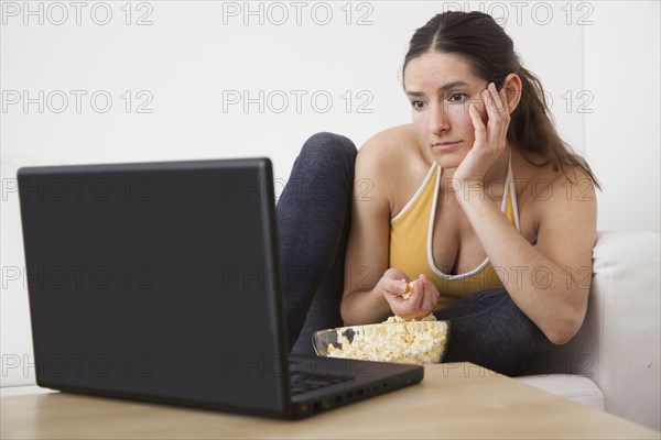 Caucasian woman eating popcorn at laptop