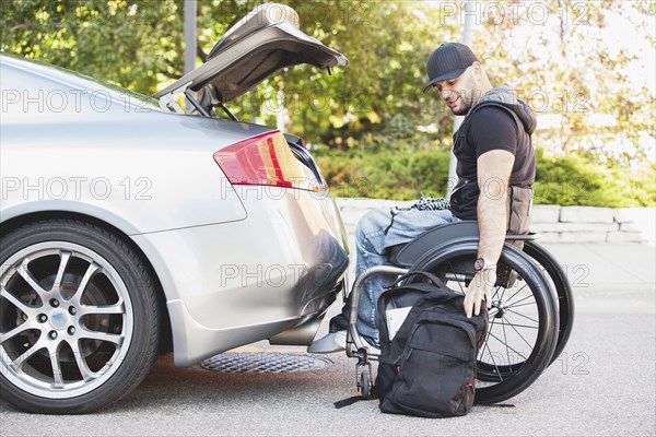 Disabled man in wheelchair packing car trunk