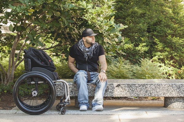 Disabled man and wheelchair sitting on stone bench