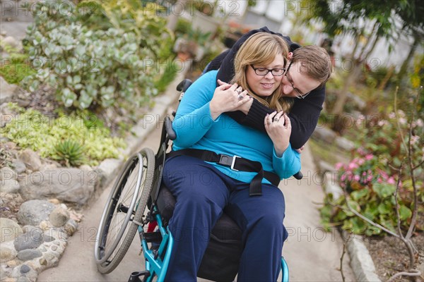 Man hugging paraplegic girlfriend in garden