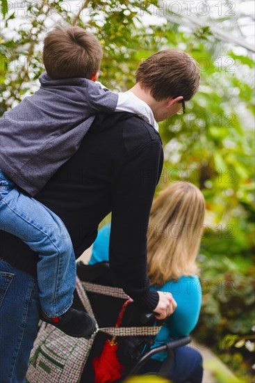 Man pushing paraplegic wife and carrying son piggyback