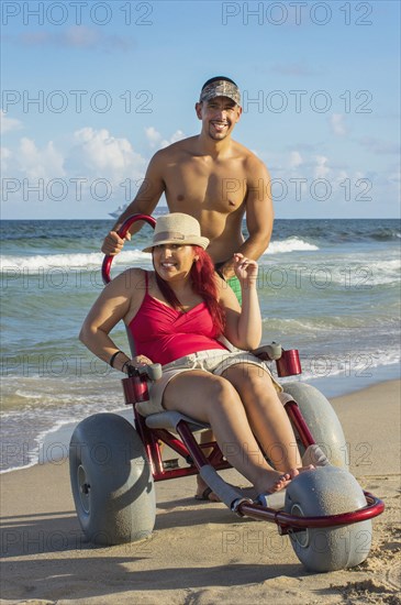 Man pushing paraplegic girlfriend in wheelchair on beach