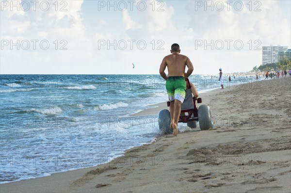 Man pushing paraplegic girlfriend in wheelchair on beach