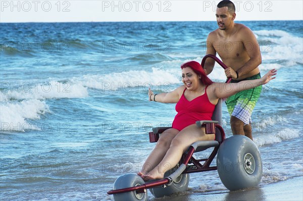 Man pushing paraplegic girlfriend in wheelchair on beach