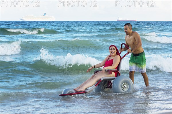 Man pushing paraplegic girlfriend in wheelchair on beach