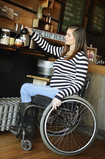 Paraplegic woman in wheelchair pouring coffee in cafe