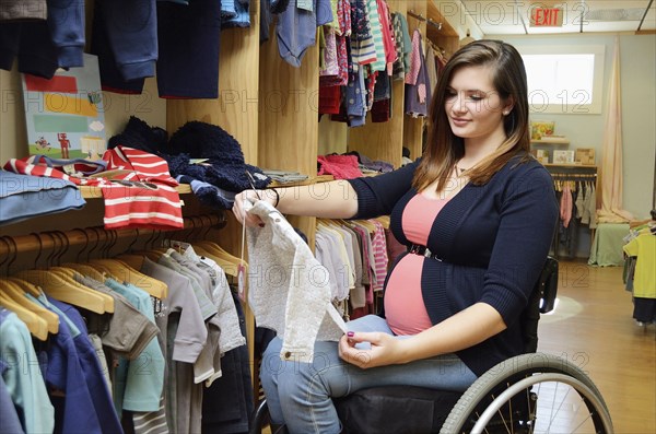 Pregnant paraplegic woman in wheelchair shopping in baby store