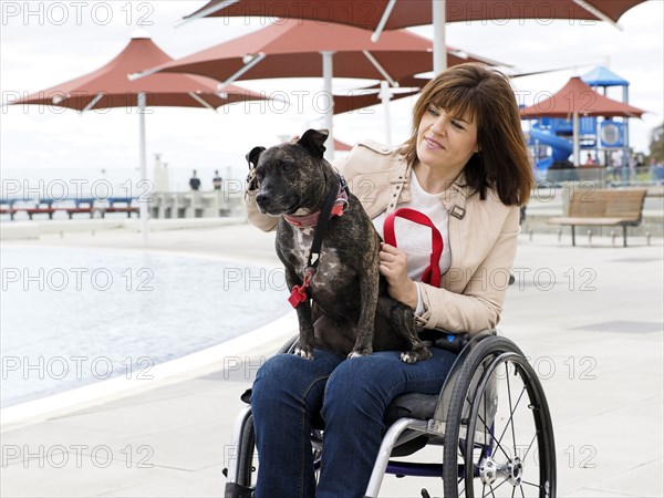 Woman sitting in wheelchair at waterfront with dog in lap