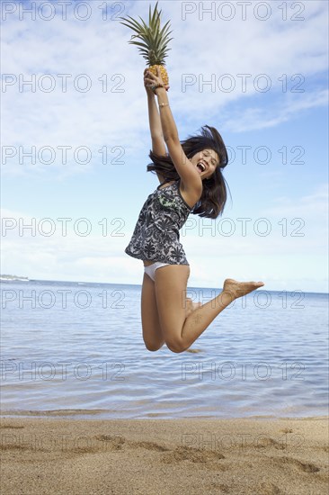 Mixed race teenager jumping and holding pineapple on beach