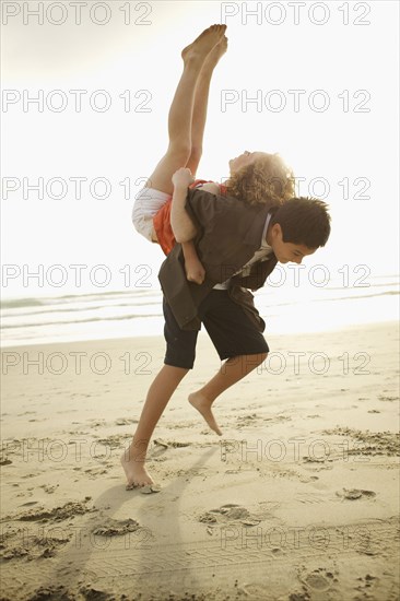 Boy lifting girl on back on beach