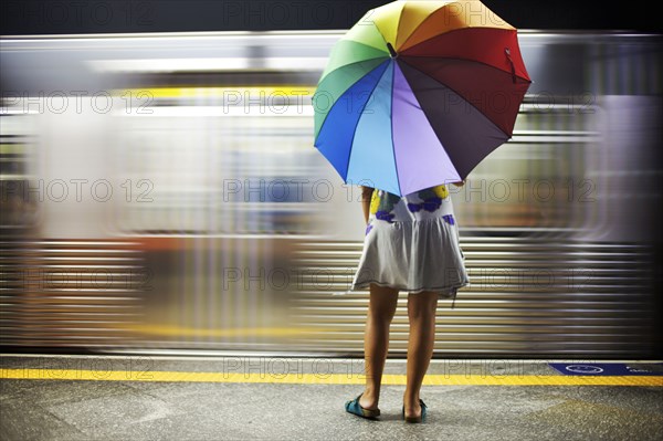 Mixed race woman with umbrella on train platform