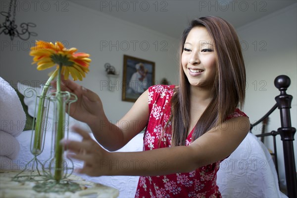 Smiling mixed race teenage girl placing flowers in vases on bedside table