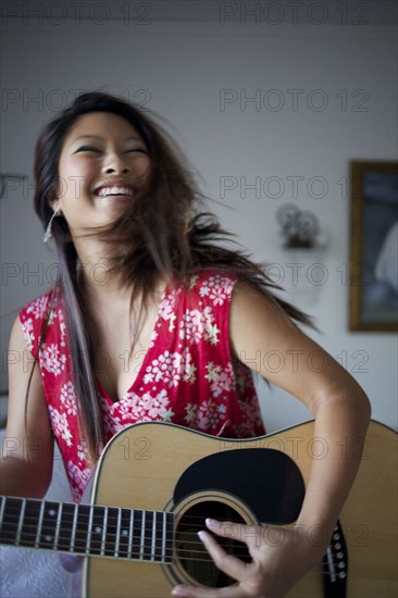 Smiling mixed race teenage girl playing guitar