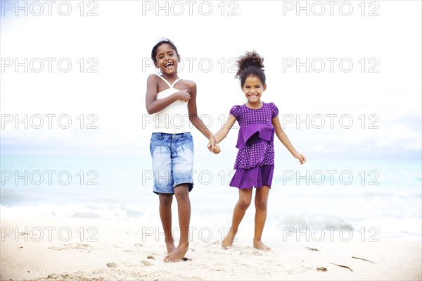 Mixed race sisters holding hands on beach