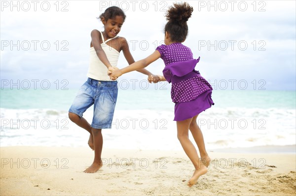 Mixed race sisters holding hands playing on beach