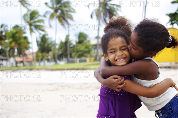 Mixed race sisters hugging on beach