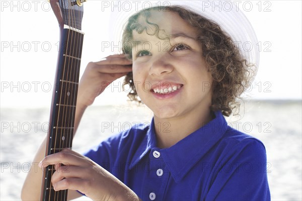 Mixed race boy holding guitar on beach