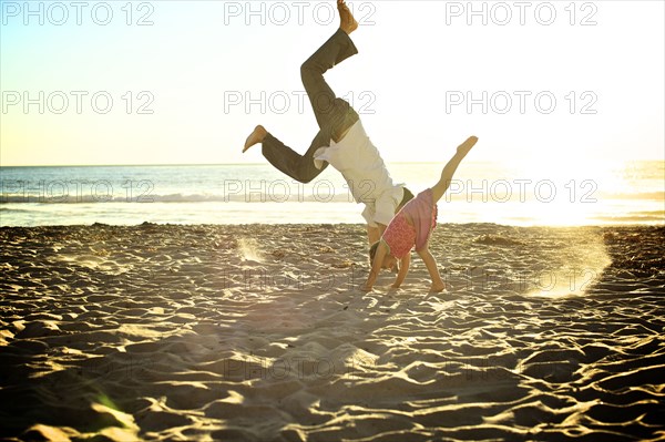 Father and daughter doing cartwheels on beach