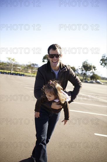 Father carrying daughter in parking lot