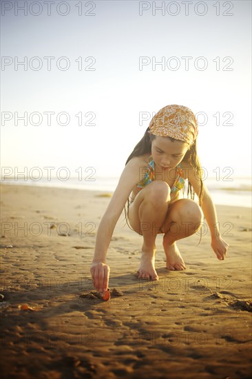 Mixed race girl digging in sand on beach