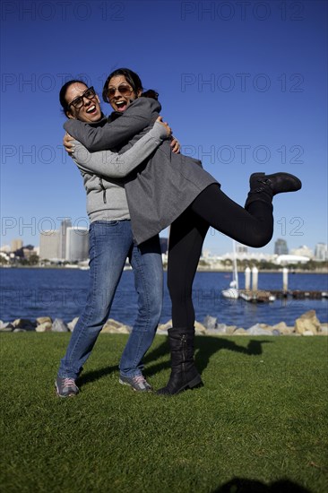 Grinning mixed race sisters hugging outdoors