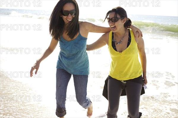 Grinning mixed race sisters hugging on beach