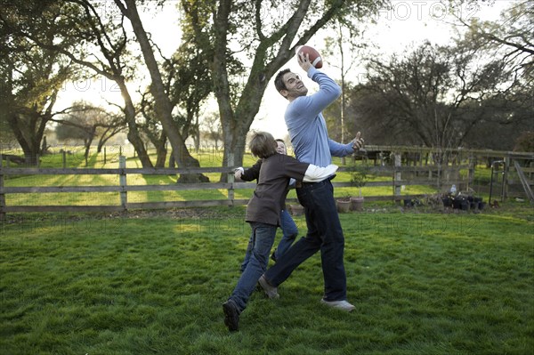 Caucasian father and sons playing football in yard