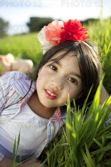 Mixed race girl with flower in hair laying in grass