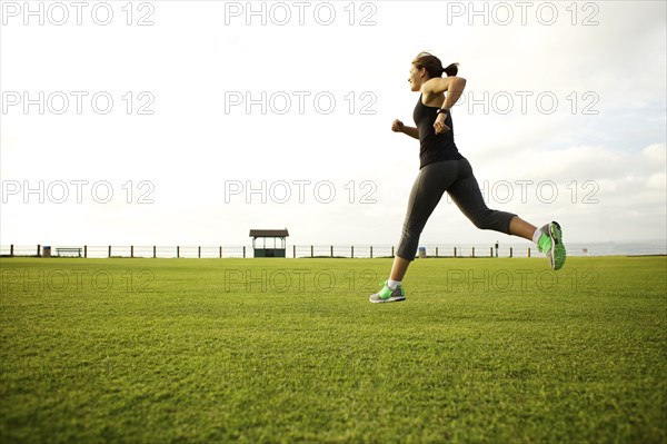 Mixed race woman running in park field