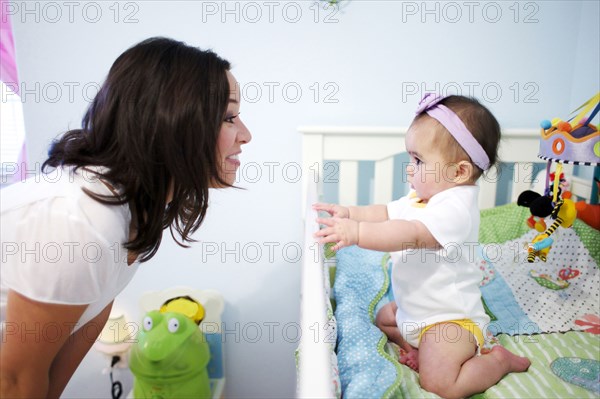Mixed race mother looking at baby girl in crib