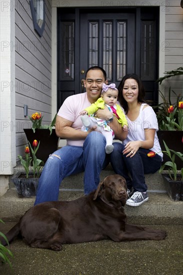 Mother and father sitting on front stoop with baby girl and dog