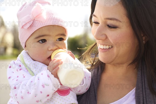 Mixed race mother watching baby girl drinking bottle