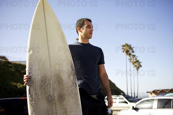 Man holding surfboard in parking lot