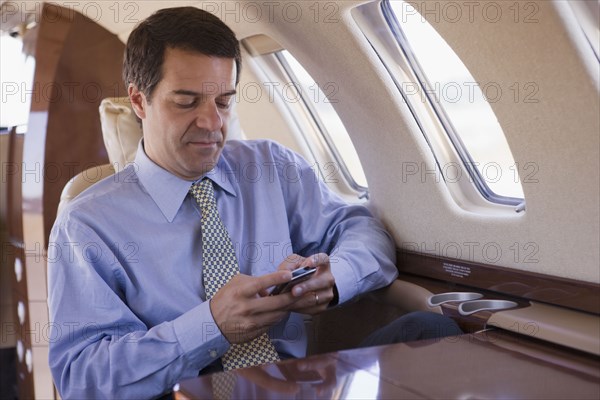 Hispanic businessman using cell phone on airplane