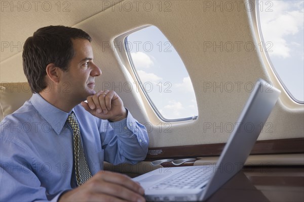 Hispanic businessman with laptop looking out airplane window