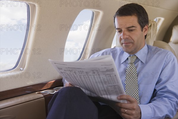 Hispanic businessman reading newspaper on airplane