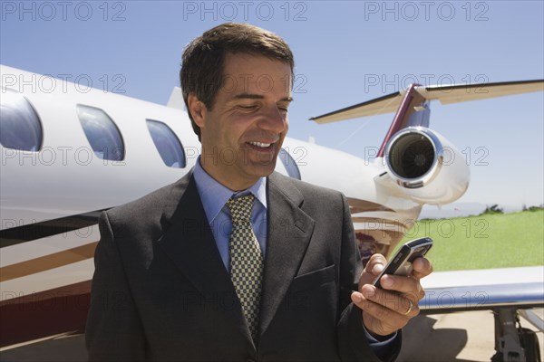 Hispanic businessman text messaging next to private jet