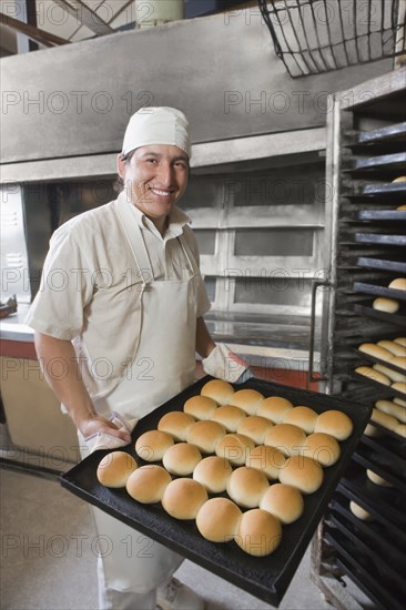 Hispanic baker holding tray with bread