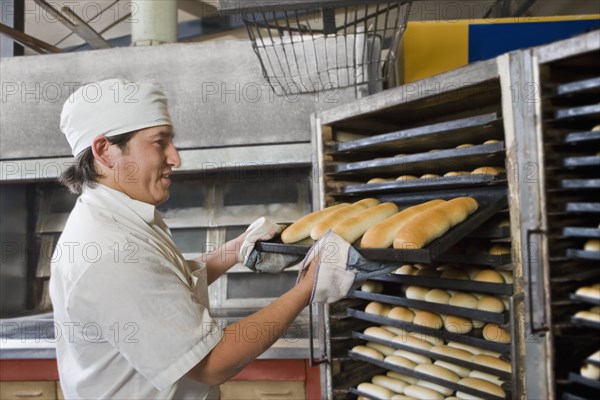 Hispanic baker holding tray with bread