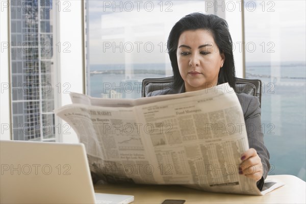 Hispanic businesswoman reading newspaper in office