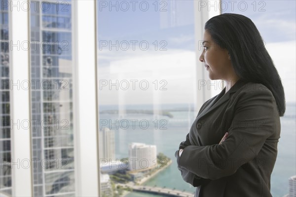 Hispanic businesswoman with arms crossed near window