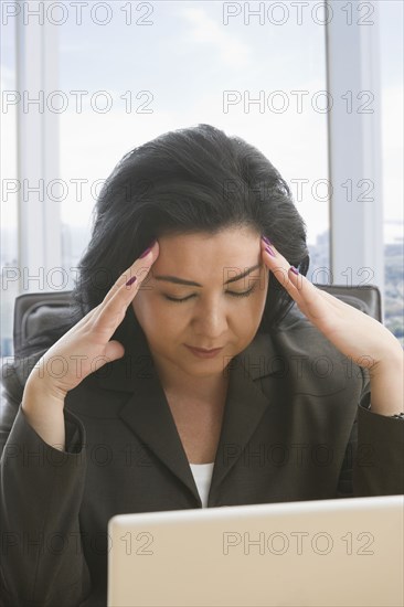 Hispanic businesswoman with headache using laptop