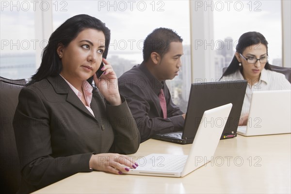 Business people in meeting using cell phone and laptops