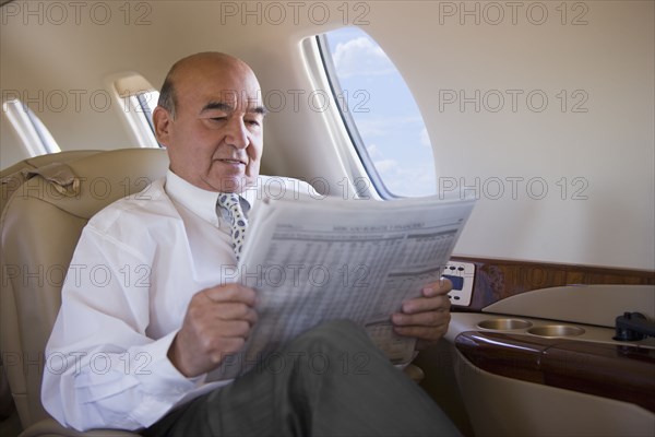 Hispanic businessman reading newspaper on private jet