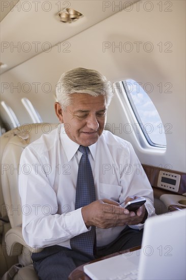 Hispanic businessman using cell phone on private jet