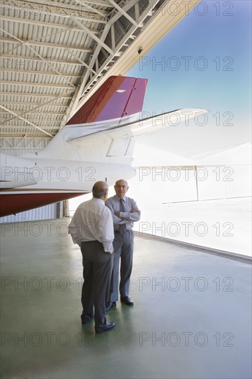 Hispanic businessmen standing in airplane hangar