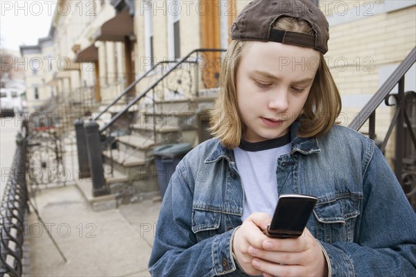 Caucasian boy text messaging on cell phone on sidewalk