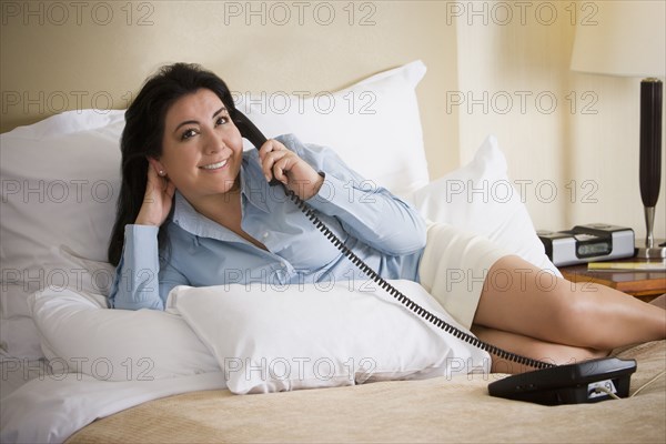 Chilean businesswoman laying on bed talking on telephone