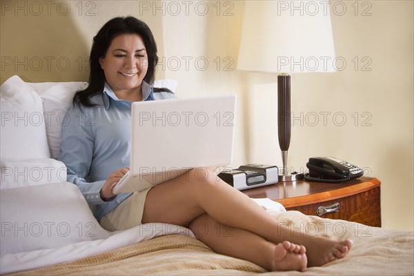 Chilean businesswoman sitting on bed using laptop