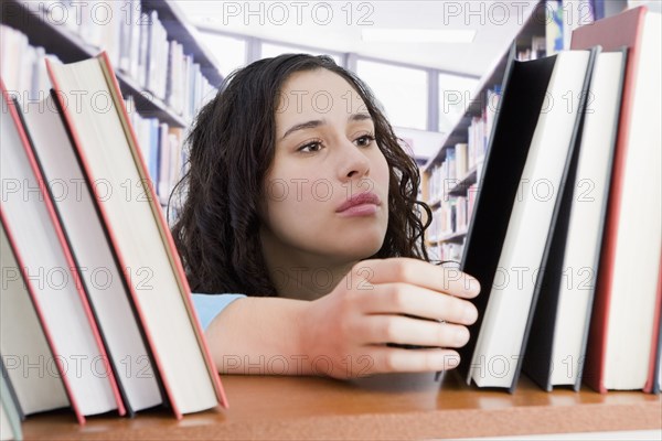 Mixed race woman looking for book in library